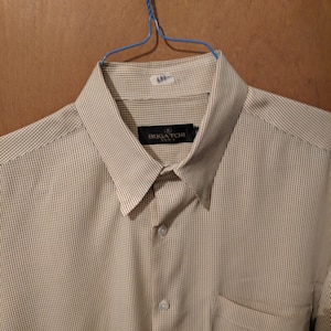 May include: A beige and brown striped dress shirt with a white collar and a pocket on the left side. The shirt has a label that says "BUGATCHI" on it.
