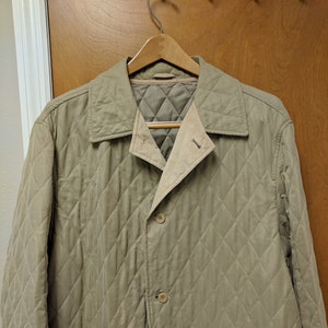 May include: A beige quilted jacket with a button closure and a single pocket on the front.