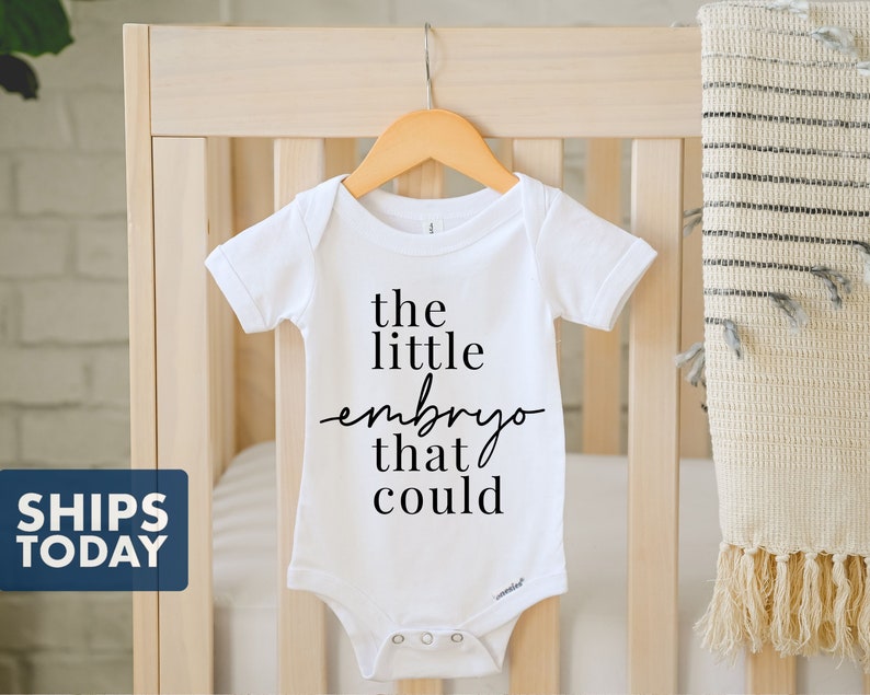 Peut inclure: Combinaison blanche pour b&eacute;b&eacute; avec un texte noir qui dit "the little embryo that could".