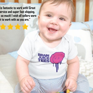 May include: A baby wearing a white onesie with a purple and pink brain graphic and the text "BRAIN JUICE TEES". The baby is sitting on a striped blanket and smiling.
