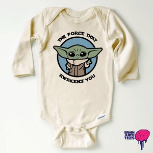 May include: A cream-colored long-sleeved baby onesie with a green alien character and the text "The Force That Awakens You".