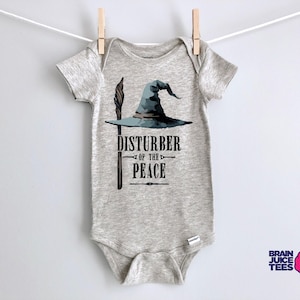 May include: A gray baby onesie with a graphic of a wizard's hat and wand. The text "Disturber of the Peace" is printed below the graphic.