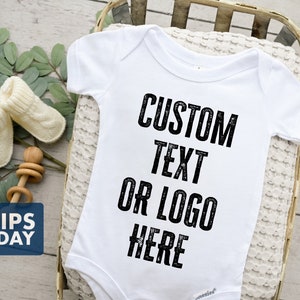 May include: White baby onesie with black text that reads "CUSTOM TEXT OR LOGO HERE" in a distressed font.