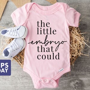 Peut inclure: Combinaison rose pour b&eacute;b&eacute; avec le texte "the little embryo that could" en noir.