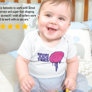 Peut inclure: Un b&eacute;b&eacute; portant un body blanc avec un motif de cerveau violet et rose et le texte "BRAIN JUICE TEES". Le b&eacute;b&eacute; est assis sur une couverture ray&eacute;e et sourit.