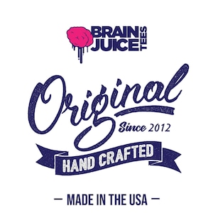 Peut inclure: Un logo bleu marine et blanc avec le texte "Brain Juice Tees" et un graphique de cerveau rose. Le texte "Original Since 2012" est sous le logo. Un ruban bleu marine avec le texte "Hand Crafted" est sous le texte. Le texte "Made in the USA" est sous le ruban.