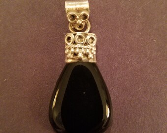 May include: A black onyx pendant with a silver bail and ornate design. The pendant is teardrop shaped and has a polished finish.