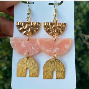 Puede incluir: Pendientes geométricos dorados y rosados con un diseño de metal texturizado y martillado. Los pendientes tienen tres niveles: un semicírculo, un semicírculo más grande y un arco curvo.