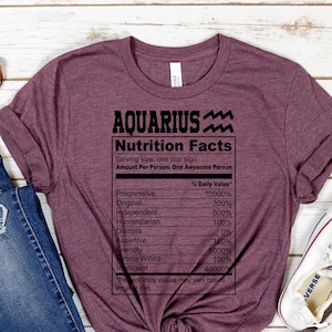 May include: A maroon t-shirt with the text "AQUARIUS Nutrition Facts" and a list of personality traits with percentages. The text is in black and the shirt is folded and tied in a knot.