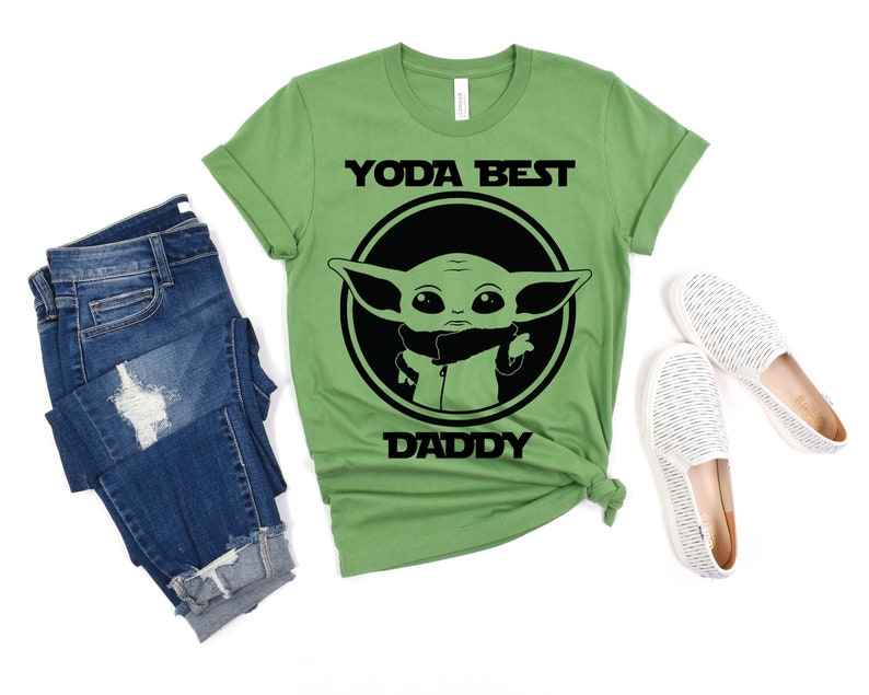 K&ouml;nnte beinhalten: Gr&uuml;nes T-Shirt mit einem schwarzen Kreis-Motiv, das eine Comicfigur mit dem Text "Yoda Best Daddy" zeigt.
