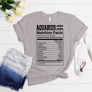 May include: Gray t-shirt with a black graphic of a nutrition facts label for Aquarius. The label lists traits like progressive, original, independent, humanitarian, disciple, assertive, friendly, strong-willed, and intelligent with a percentage value for each.