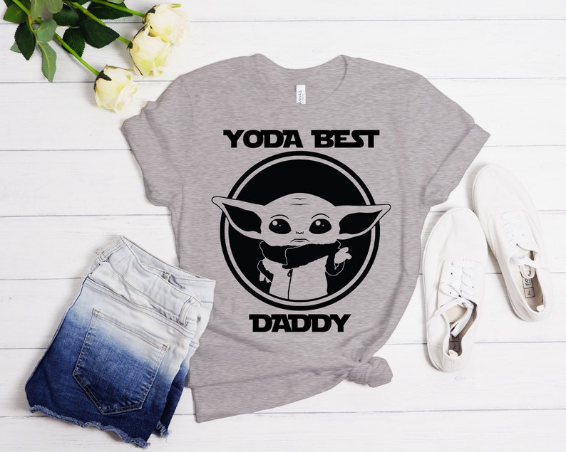 K&ouml;nnte beinhalten: Graues T-Shirt mit einer schwarz-wei&szlig;en Grafik eines Charakters aus dem Star Wars-Franchise. Der Text "YODA BEST DADDY" ist auf dem T-Shirt aufgedruckt.