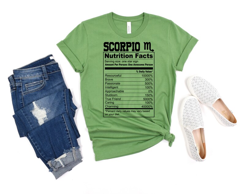 May include: Green t-shirt with a black graphic of a nutrition facts label for the zodiac sign Scorpio. The label lists traits like resourceful, brave, passionate, intelligent, approachable, stubborn, true friend, caring, and charming with a percentage value for each.