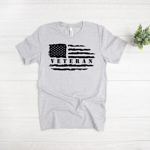 Może przedstawiać: Szary T-shirt z nadrukowaną czarną, przetartą flagą amerykańską i napisem "Veteran".