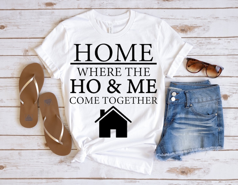 May include: White t-shirt with black text that reads "HOME WHERE THE HO & ME COME TOGETHER" and a black silhouette of a house.