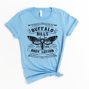 May include: Light blue t-shirt with a black graphic of a moth and text that reads "It rubs the lotion on its Buffalo Bill's. Comes with its own free basket! Body Lotion. Skin or else it gets the hose again."