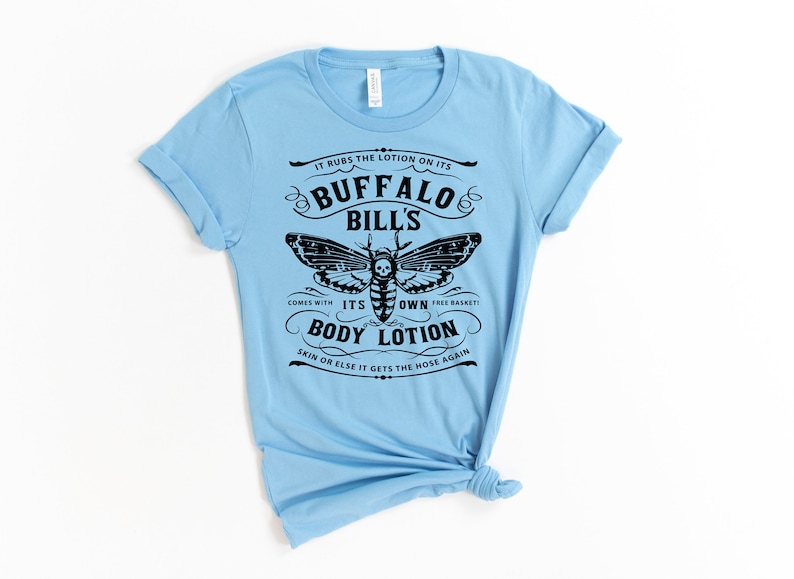 May include: Light blue t-shirt with a black graphic of a moth and text that reads "It rubs the lotion on its Buffalo Bill's. Comes with its own free basket! Body Lotion. Skin or else it gets the hose again."