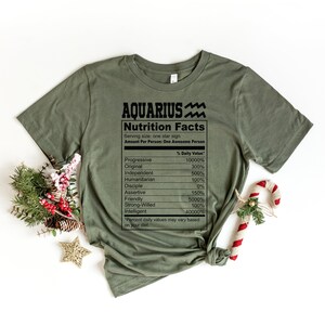 May include: A green t-shirt with a nutrition facts label for the zodiac sign Aquarius. The label lists traits like progressive, original, independent, humanitarian, disciple, assertive, friendly, strong-willed, and intelligent.