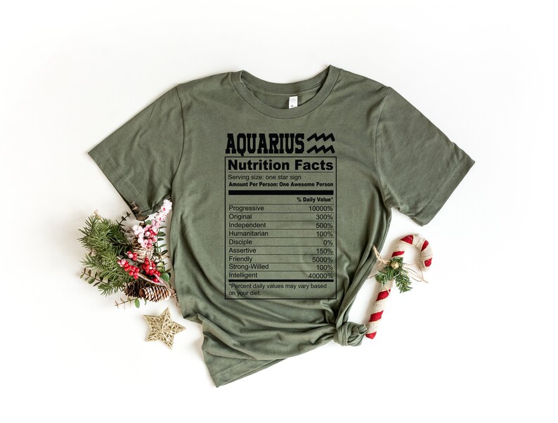 May include: A green t-shirt with a nutrition facts label for the zodiac sign Aquarius. The label lists traits like progressive, original, independent, humanitarian, disciple, assertive, friendly, strong-willed, and intelligent.