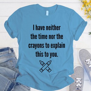 May include: A light blue t-shirt with the text "I have neither the time nor the crayons to explain this to you." and a black and white illustration of two crossed crayons.
