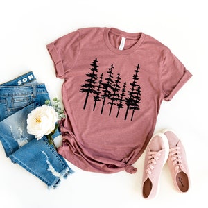 May include: Mauve-colored t-shirt with a black tree silhouette design. The image also includes blue denim jeans, a white flower, and pink sneakers. The t-shirt is knotted at the waist.
