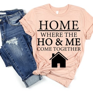 May include: A peach-colored t-shirt with black text that reads "HOME WHERE THE HO & ME COME TOGETHER" and a black silhouette of a house.