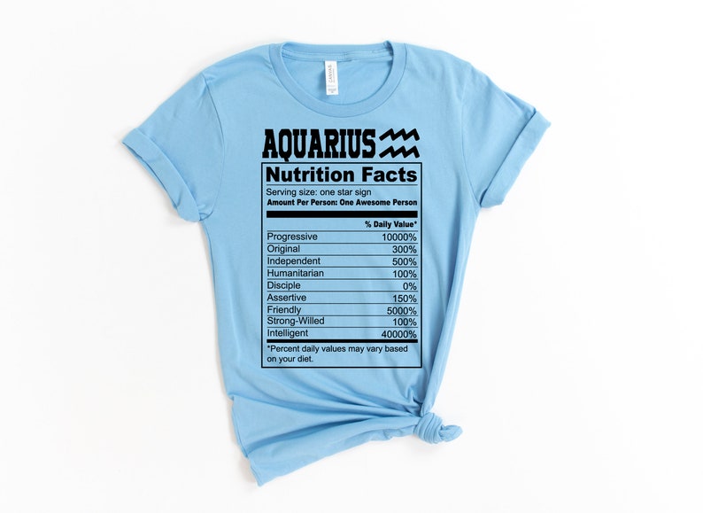 May include: A light blue t-shirt with a black graphic of a nutrition facts label for Aquarius. The label lists traits like "Progressive", "Original", "Independent", and "Intelligent" with percentages next to each trait.