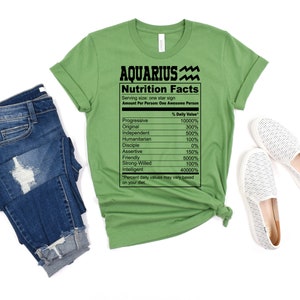 May include: Green t-shirt with a black graphic of a nutrition facts label for Aquarius. The label lists traits like progressive, original, independent, humanitarian, disciple, assertive, friendly, strong-willed, and intelligent with a percentage daily value for each.