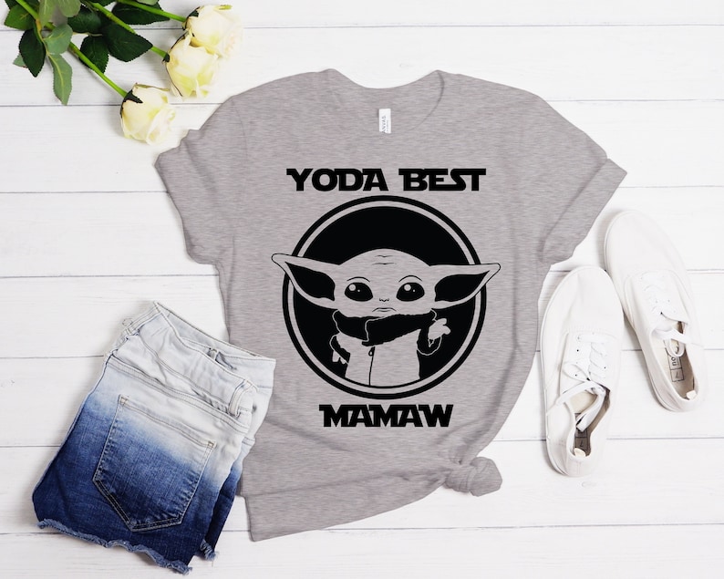 May include: Gray t-shirt with a black and white graphic of a character from Star Wars: The Mandalorian. The text "Yoda Best Mamaw" is printed on the shirt.