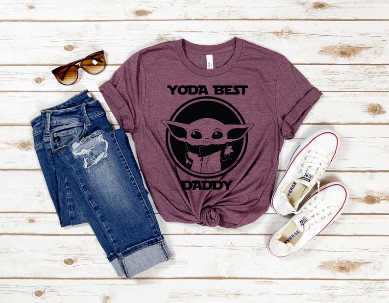 K&ouml;nnte beinhalten: Ein maronfarbenes T-Shirt mit einer schwarzen Grafik eines Charakters aus dem Star Wars-Franchise. Die Grafik lautet "Yoda Best Daddy".