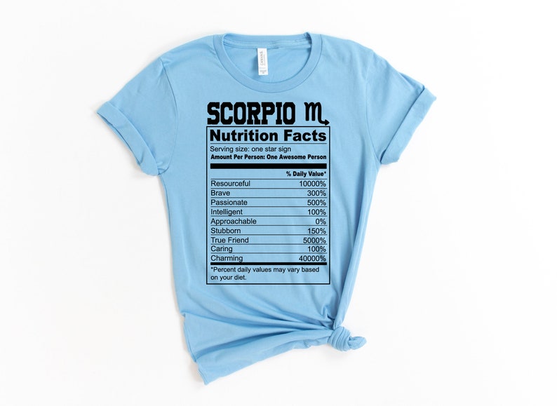 May include: Light blue t-shirt with a black graphic of a nutrition facts label for Scorpio. The label lists traits like resourceful, brave, passionate, intelligent, approachable, stubborn, true friend, caring, and charming with a percentage value for each.