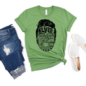 May include: Green t-shirt with a black and white graphic of Elvis Presley's face made up of words related to his music. The words include "Hound Dog", "Jailhouse Rock", "Can't Help Falling in Love", and "Suspicious Minds".