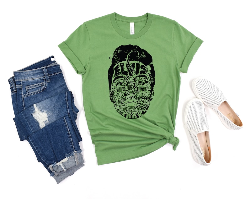 May include: Green t-shirt with a black and white graphic of Elvis Presley's face made up of words related to his music. The words include "Hound Dog", "Jailhouse Rock", "Can't Help Falling in Love", and "Suspicious Minds".