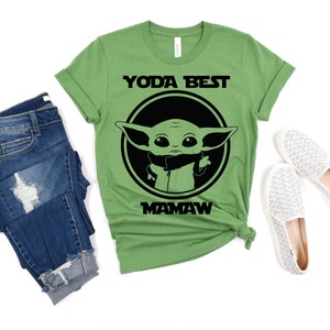 May include: Green t-shirt with a black and white graphic of a baby Yoda character. The text "Yoda Best Mamaw" is printed on the shirt.