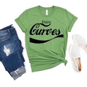 May include: A green t-shirt with the text "Enjoy Curves" in a black, stylized font that resembles a popular soda brand logo.
