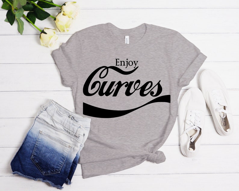 May include: A gray t-shirt with the text "Enjoy Curves" in a black, stylized font that resembles a Coca-Cola logo.