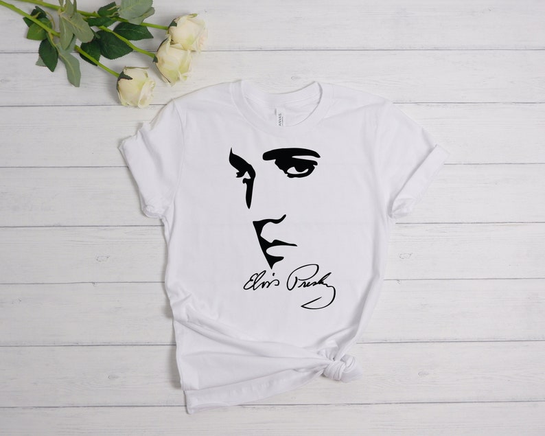 May include: White t-shirt with a black silhouette of Elvis Presley's face and his signature.