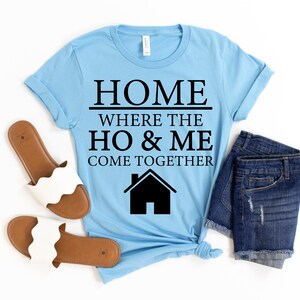 May include: Light blue t-shirt with black text that reads "Home where the ho & me come together" and a black silhouette of a house.