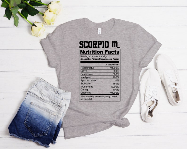 May include: Gray t-shirt with a black graphic of a nutrition facts label for Scorpio. The label lists traits like resourceful, brave, passionate, intelligent, approachable, stubborn, true friend, caring, and charming with percentages next to each trait.