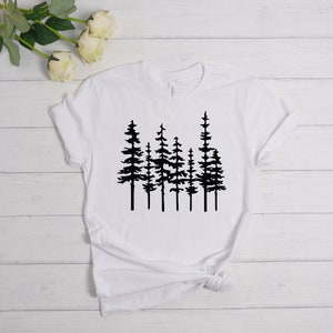 May include: White t-shirt featuring a black graphic of several stylized pine trees. The trees are depicted with detailed silhouettes, creating a nature-inspired design. The shirt is made of a soft material and has a classic crew neck.