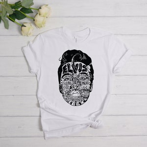 May include: White t-shirt with a black and white graphic of Elvis Presley's face made up of words related to his music and career. The words include "Hound Dog", "Jailhouse Rock", "Love Me Tender", and "Can't Help Falling in Love".