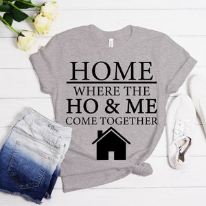 May include: A gray t-shirt with black text that reads "HOME WHERE THE HO & ME COME TOGETHER" and a black house icon.