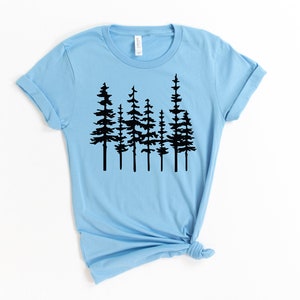 May include: Light blue t-shirt featuring a black graphic of several stylized pine trees. The shirt has short sleeves and a crew neck. The bottom of the shirt is tied in a knot.