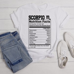 May include: White t-shirt with a black graphic of a nutrition facts label for a Scorpio. The label lists traits like resourceful, brave, passionate, intelligent, approachable, stubborn, true friend, caring, and charming with a percentage value for each.