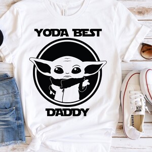 K&ouml;nnte beinhalten: Wei&szlig;es T-Shirt mit einer schwarz-wei&szlig;en Grafik eines Star Wars-Charakters, "Yoda Best Daddy".