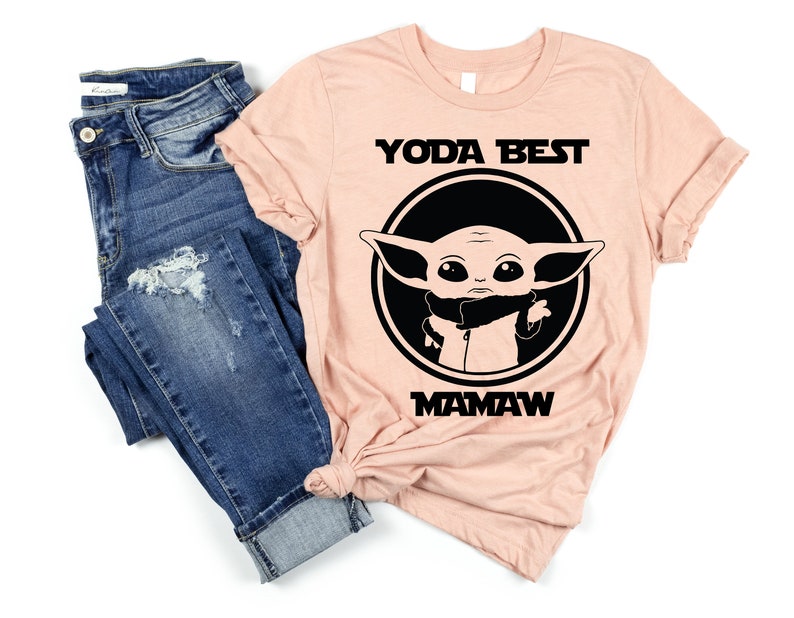 May include: A peach-colored t-shirt with a black circle containing a cartoon image of Baby Yoda. The text "YODA BEST MAMA W" is printed in black below the circle.