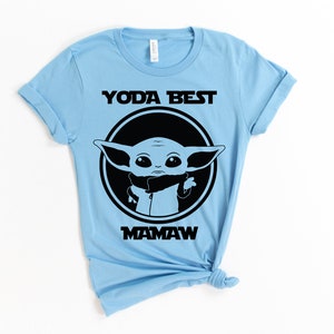 May include: Light blue t-shirt with a black graphic of a cartoon character from the Star Wars franchise. The text "Yoda Best Mamaw" is printed on the shirt.