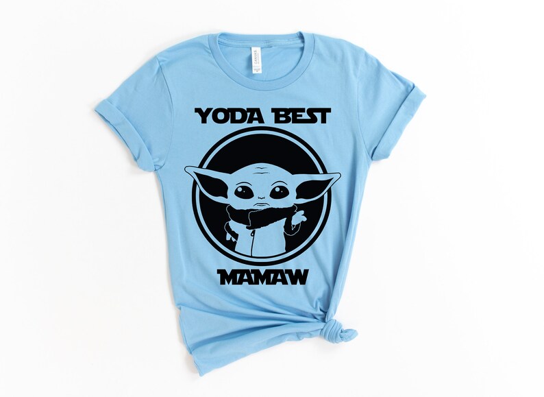 May include: Light blue t-shirt with a black graphic of a cartoon character from the Star Wars franchise. The text "Yoda Best Mamaw" is printed on the shirt.