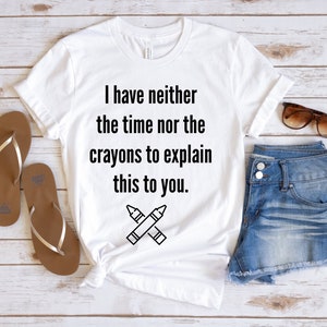 May include: White t-shirt with a black graphic that says "I have neither the time nor the crayons to explain this to you." and a pair of crossed crayons.
