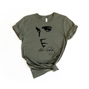 May include: A green t-shirt with a black silhouette of Elvis Presley's face and his signature.